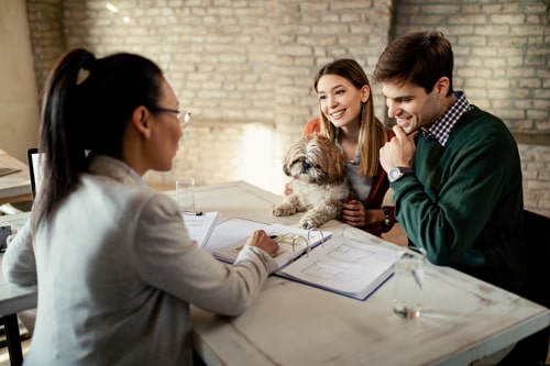 Young Happy Couple Analyzing Plans With Their Real Estate Agent While Having Meeting Office Min